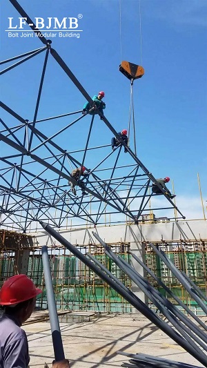 LF-BJMB workers carry out lifting and erection of large-span spherical node steel roof on construction site. Insufficient pre-fabrication engineering coordination will cause component matching defects, crane downtime and schedule delays; early constructability review and factory pre-assembly eliminate such hidden installation risks.