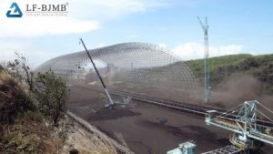 Erection of a bolted space frame storage shed — prefabricated members assembled with cranes at a bulk material yard.